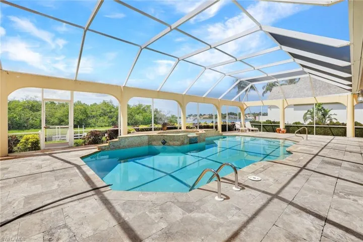 View of large screen enclosed lanai with a spacious pool featuring a spill over spa, views out to Naples Bay.