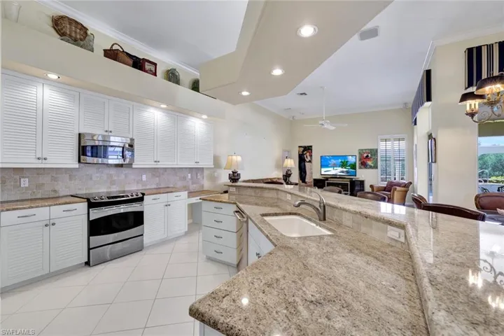 Kitchen with appliances with stainless steel finishes, decorative backsplash, sink, light stone countertops, and white cabinets, and pantry.
