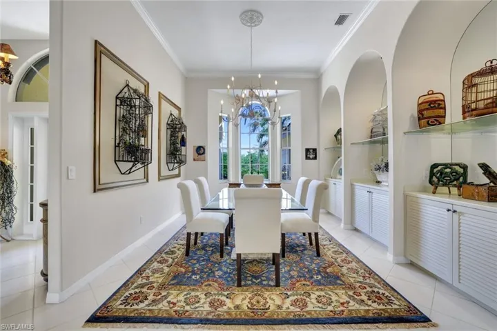 Formal dining area featuring ornamental molding, a chandelier, light tile floors, and built in shelves with cabinets.