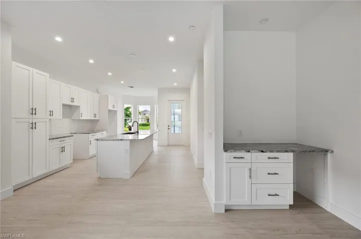 Kitchen featuring white cabinets, an island with sink, light stone countertops, tasteful backsplash, and a breakfast bar area