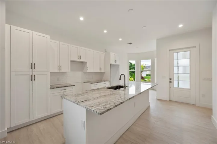 Kitchen with light stone counters, white cabinets, backsplash, a kitchen island with sink, and recessed lighting