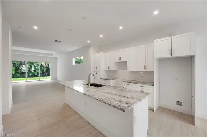 Kitchen featuring light stone countertops, white cabinetry, decorative backsplash, a center island with sink, and recessed lighting