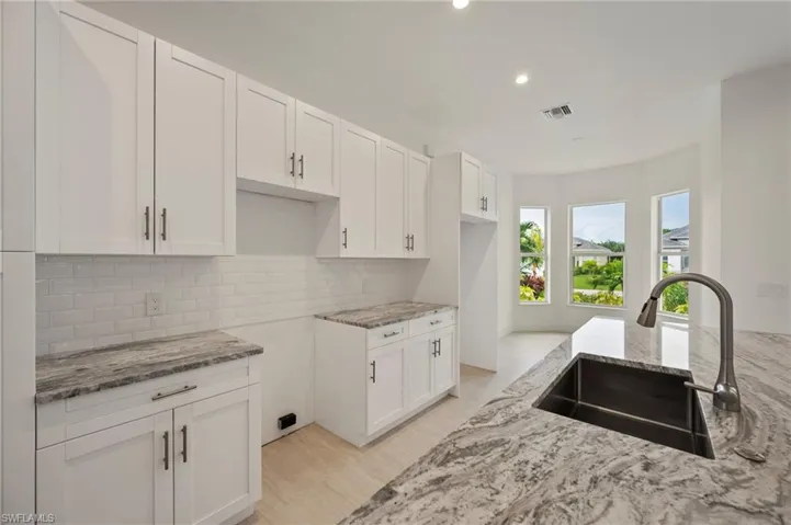 Kitchen featuring white cabinetry, light stone counters, tasteful backsplash, and recessed lighting
