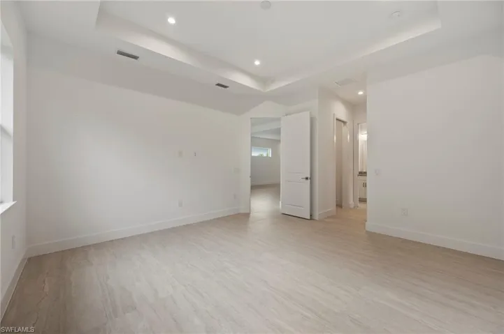 Empty room with a raised ceiling, light wood finished floors, and recessed lighting
