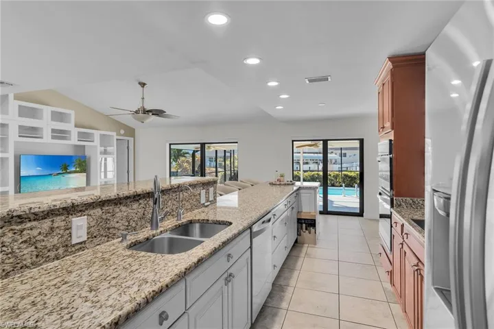 Kitchen featuring appliances with stainless steel finishes, light stone countertops, recessed lighting, light tile patterned floors, and lofted ceiling