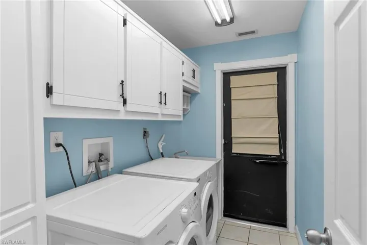 Washroom featuring washing machine and clothes dryer, cabinet space, and light tile patterned flooring