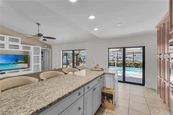 Kitchen featuring light stone counters, light tile patterned floors, lofted ceiling, a breakfast bar area, and recessed lighting