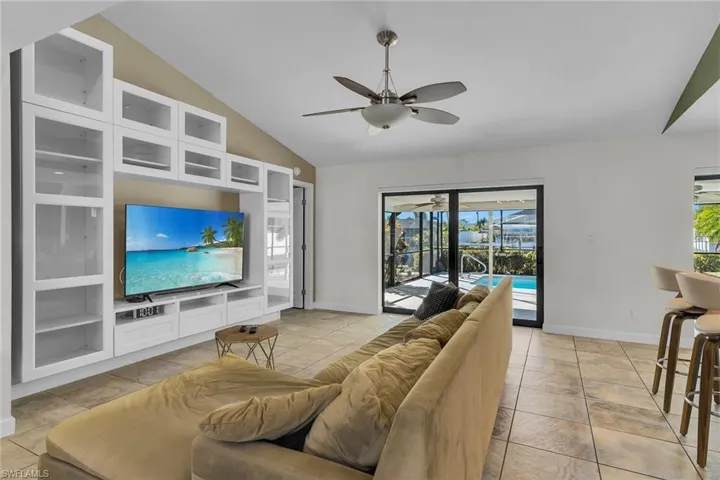 Living room with vaulted ceiling, built in shelves, light tile patterned floors, a ceiling fan, and a sunroom