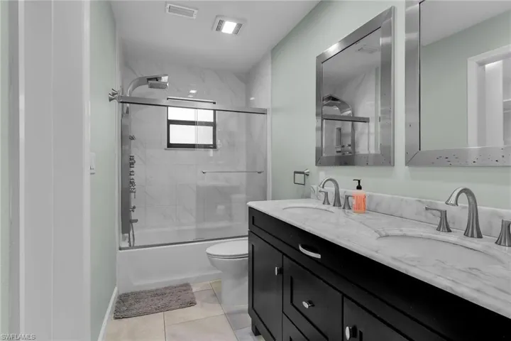 Full bathroom with bath / shower combo with glass door, double vanity, and light tile patterned floors