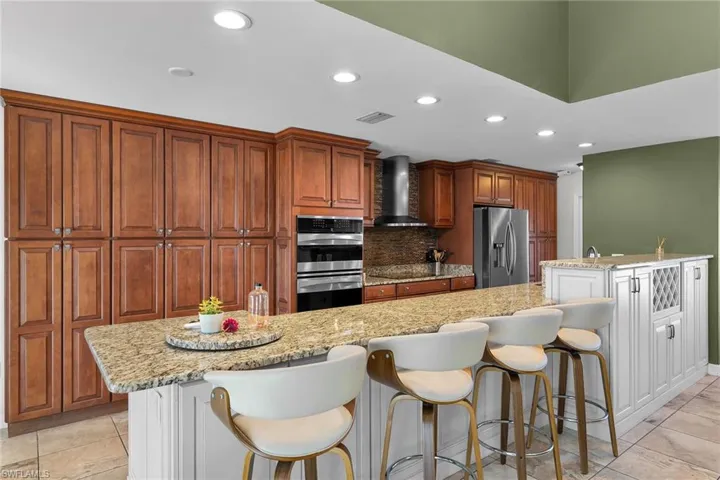 Kitchen with a spacious island, light stone countertops, stainless steel appliances, recessed lighting, and light tile patterned flooring