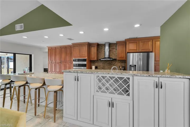 Kitchen featuring backsplash, recessed lighting, light stone counters, brown cabinets, and a breakfast bar area