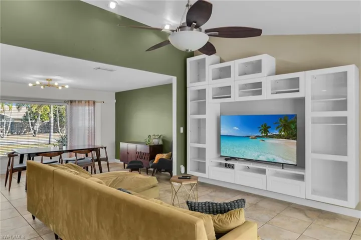 Living room with ceiling fan, light tile patterned floors, a chandelier, and lofted ceiling