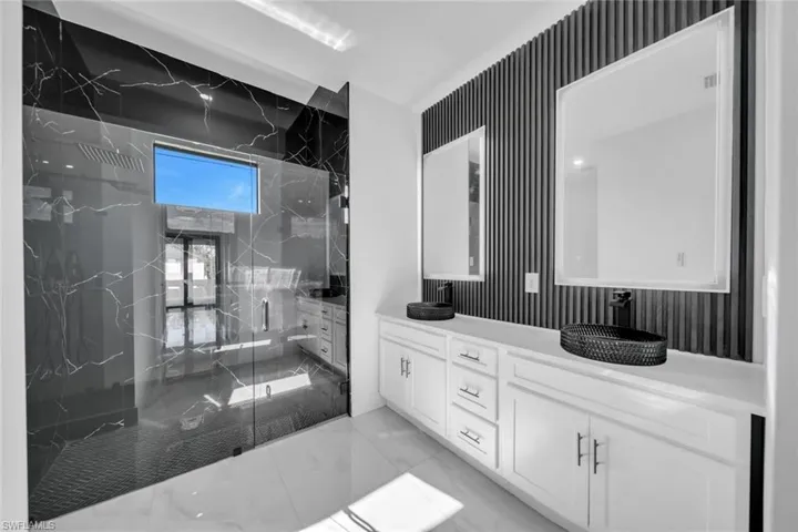 Full bath featuring double vanity, a marble finish shower, wallpapered walls, and light marble finish floors