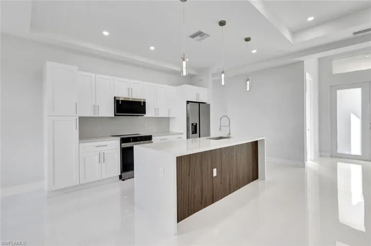 Kitchen with white cabinets, appliances with stainless steel finishes, recessed lighting, light countertops, and an island with sink