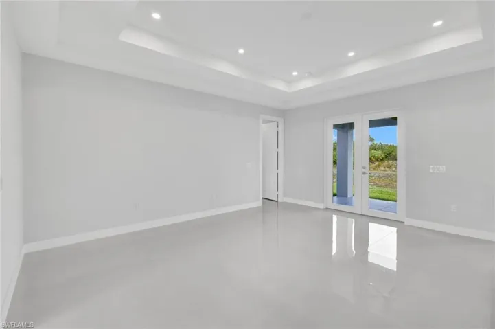 Empty room with a raised ceiling, french doors, recessed lighting, and finished concrete floors