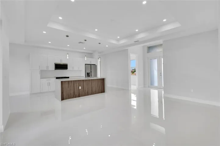 Kitchen featuring a tray ceiling, recessed lighting, white cabinets, a spacious island, and appliances with stainless steel finishes