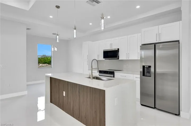 Kitchen featuring appliances with stainless steel finishes, white cabinets, light countertops, decorative light fixtures, and recessed lighting