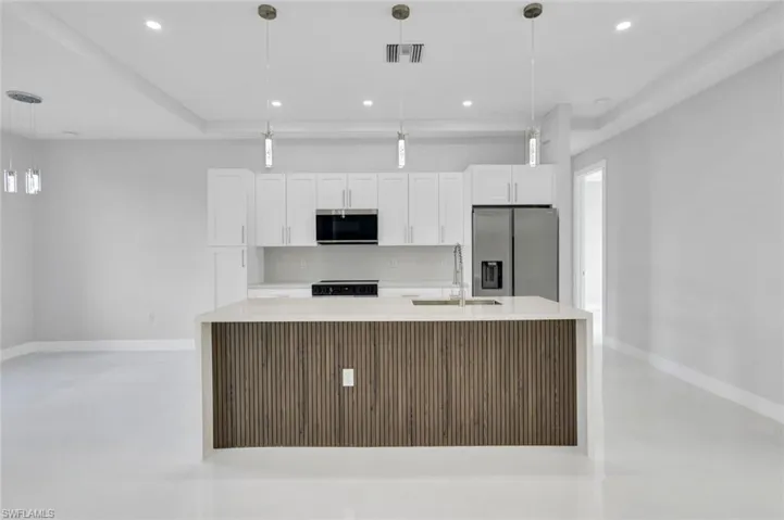 Kitchen with appliances with stainless steel finishes, a kitchen island with sink, white cabinetry, light countertops, and recessed lighting