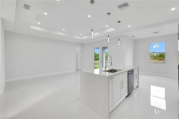Kitchen with open floor plan, recessed lighting, a tray ceiling, a center island with sink, and white cabinetry