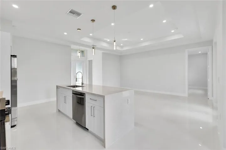 Kitchen with a raised ceiling, recessed lighting, white cabinetry, an island with sink, and open floor plan