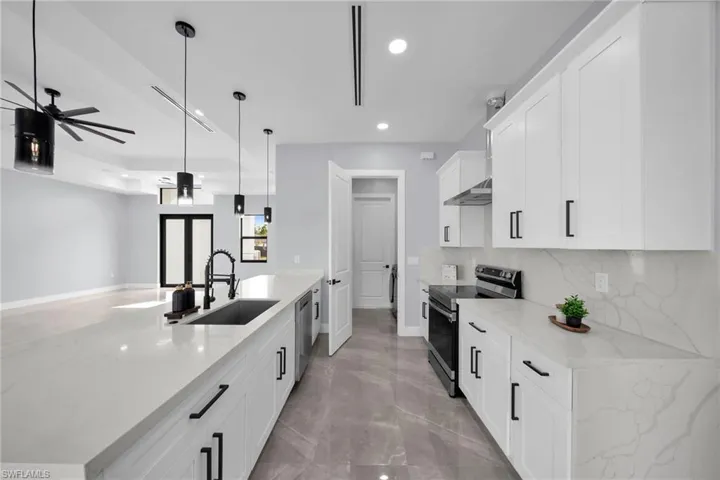 Kitchen featuring decorative light fixtures, white cabinets, light stone counters, and stainless steel appliances