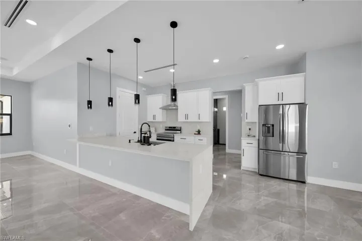 Kitchen with appliances with stainless steel finishes, sink, white cabinetry, and decorative light fixtures
