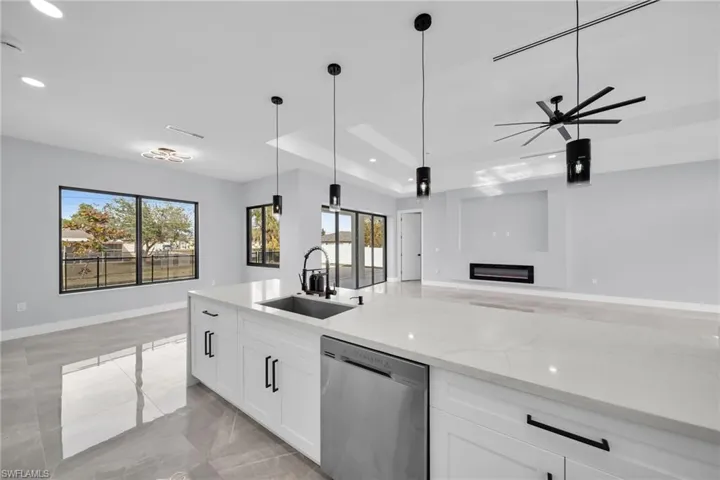 Kitchen featuring light stone countertops, white cabinets, sink, hanging light fixtures, and stainless steel dishwasher
