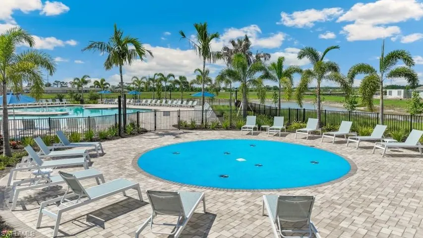 Community amenities include a vibrant outdoor splash pad surrounded by lounge chairs, a paver patio, and lush palm trees