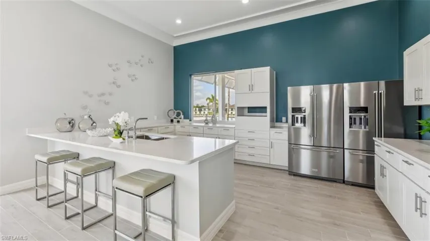 The kitchen features an island with a sink, white cabinetry, stainless steel refrigerators, and light-colored flooring