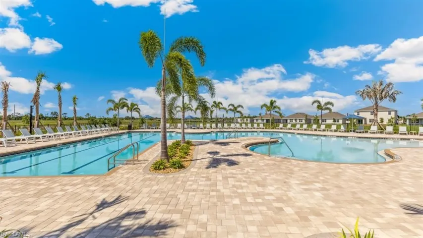 Expansive outdoor pool area featuring a large swimming pool, a separate pool with a curved edge, and a spacious paver deck with numerous lounge chairs