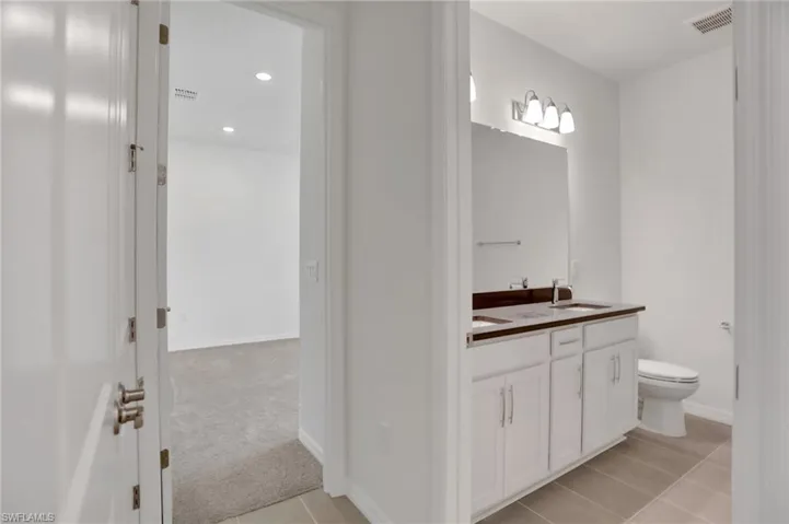 Bathroom with double vanity, light colored carpet, light tile patterned flooring, and recessed lighting