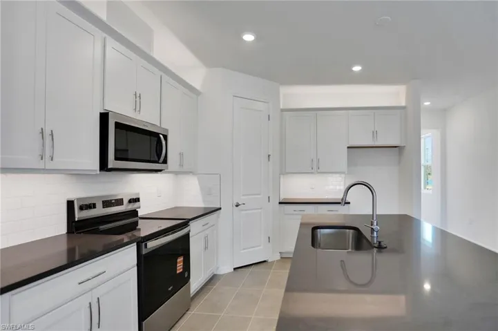 Kitchen with stainless steel appliances, white cabinetry, light tile patterned flooring, recessed lighting, and dark stone countertops