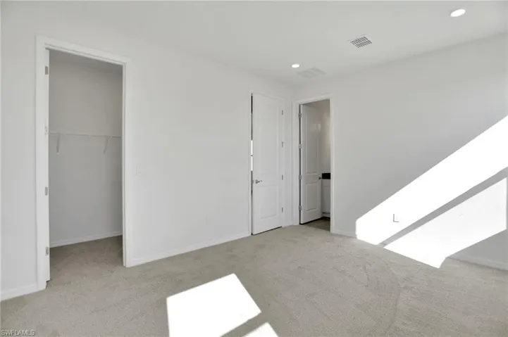 Unfurnished bedroom with a spacious closet, light colored carpet, and recessed lighting