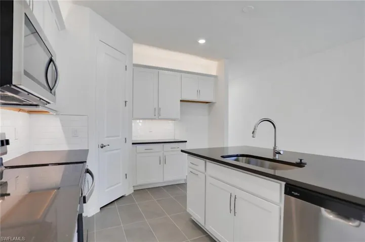 Kitchen with stainless steel appliances, white cabinets, decorative backsplash, light tile patterned flooring, and recessed lighting