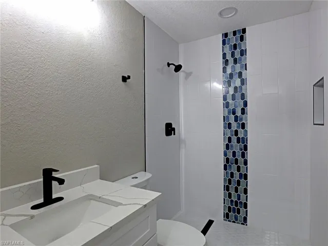 Bathroom with a textured wall, vanity, a tile shower, and a textured ceiling