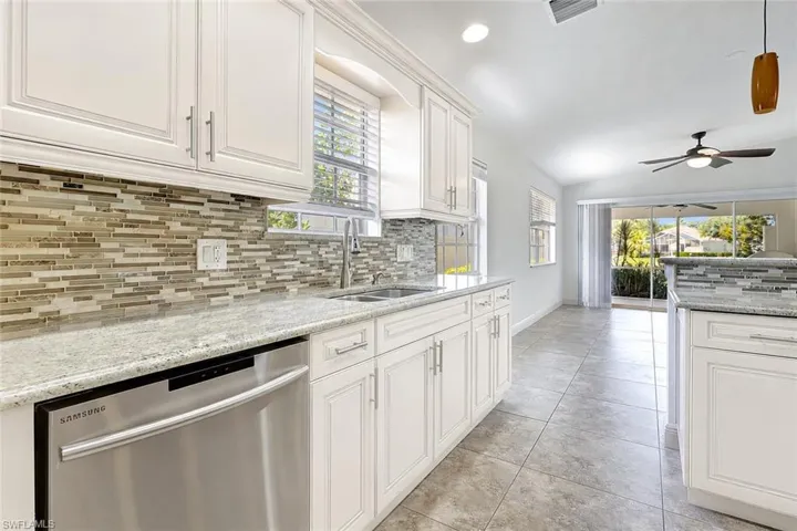 Staged photo with off-white cabinetry with brushed nickel hardware, granite countertops, and a linear mosaic tile backsplash
