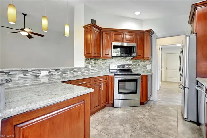Kitchen with stainless steel appliances, light stone countertops, pendant lighting.