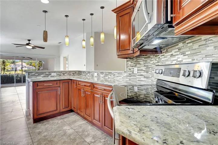 Kitchen featuring stainless steel appliances, decorative backsplash, light stone counters, decorative light fixtures, and a peninsula