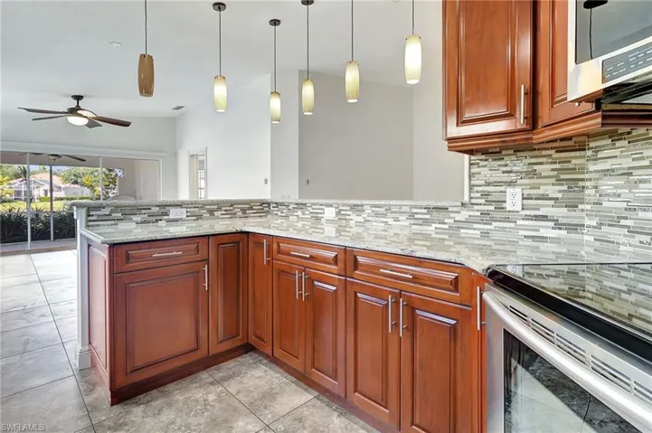 Actual condition of the Upgraded Kitchen with stainless steel appliances, hanging light fixtures, light stone countertops, a peninsula, and backsplash.