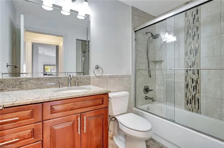 Guest bathroom featuring tile walls, vanity, bath / shower combo with glass door.
