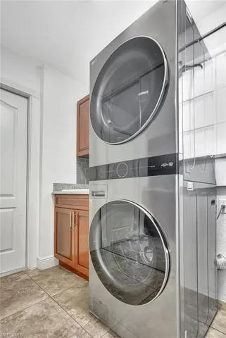 Laundry room featuring solid wood cabinet  and stacked washer / dryer, and light tile patterned flooring.