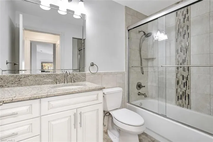 Staged photo with cabinets painted. Bathroom featuring a white vanity with a light-toned countertop, a rectangular mirror, and a shower-tub combination with sliding glass doors
