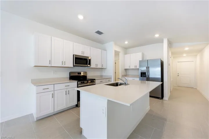 Kitchen with appliances with stainless steel finishes, white cabinetry, an island with sink, recessed lighting, and light tile patterned floors