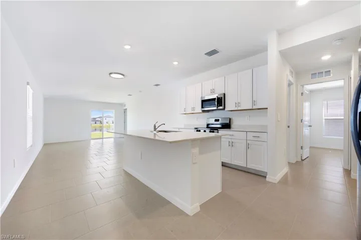 Kitchen with a kitchen island with sink, white cabinetry, appliances with stainless steel finishes, open floor plan, and healthy amount of natural light