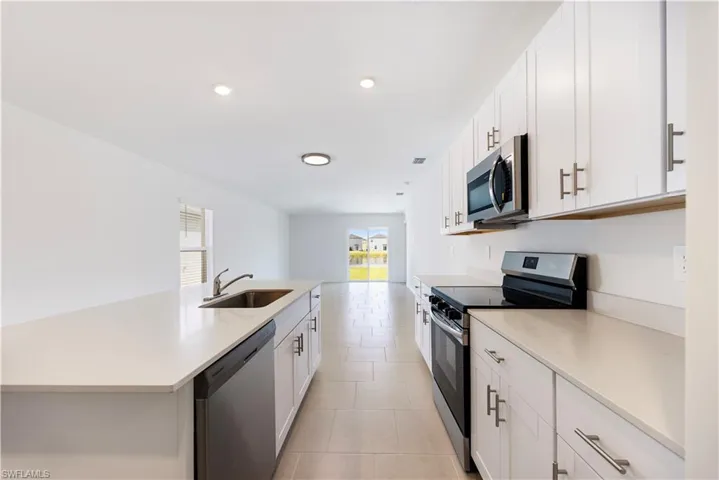 Kitchen featuring stainless steel appliances, white cabinetry, light stone counters, recessed lighting, and a center island with sink