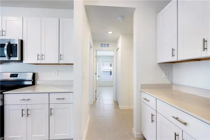 Kitchen with stainless steel appliances, white cabinets, light tile patterned floors, and light stone countertops
