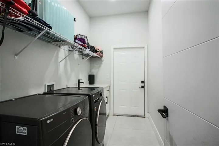 White tile flooring, built-in wire shelving, white wall paneling, counter space, and a sink with a black faucet