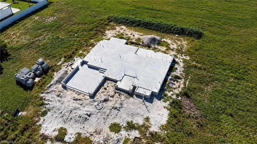 Aerial view of a residential building site featuring a poured concrete foundation, set on an expansive cleared lot