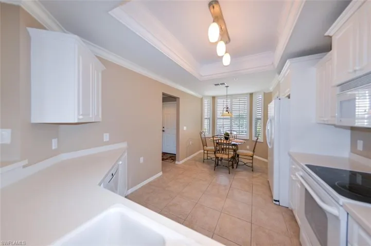 Kitchen with white cabinets, white appliances, light countertops, light tile patterned flooring, and decorative light fixtures