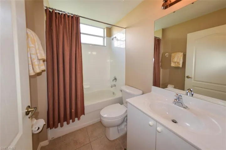 Bathroom featuring shower / bathtub combination with curtain, vanity, and light tile patterned floors